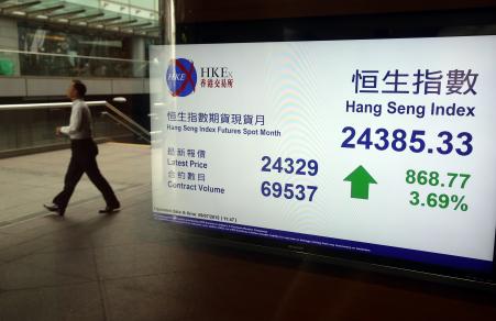 © Getty Images/AFP/Isaac Lawrence. A man walks past an electronic board displaying the Hang Seng Index at the Hong Kong Stock Exchange on July 9, 2015.