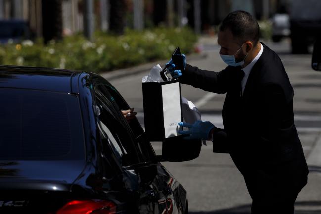 © Bloomberg. An employee wearing a protective mask and gloves hands a purchase to a customer in a vehicle at a curbside pickup location outside a Gucci Ltd. store on Rodeo Drive in Beverly Hills, California, U.S., on Tuesday, May 19, 2020. The luxury-goods market will shrink between 15% and 35% this year as the coronavirus and efforts to control it hammer sales of high-end goods, consultancy Bain forecast in a report. Photographer: Patrick T. Fallon/Bloomberg