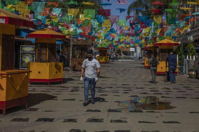 © Bloomberg. A pedestrian wearing a protective mask and gloves passes in front of closed kiosks on Santiago Arguello street in Tijuana, Mexico, on March 23. Photographer: Alejandro Cegarra/Bloomberg