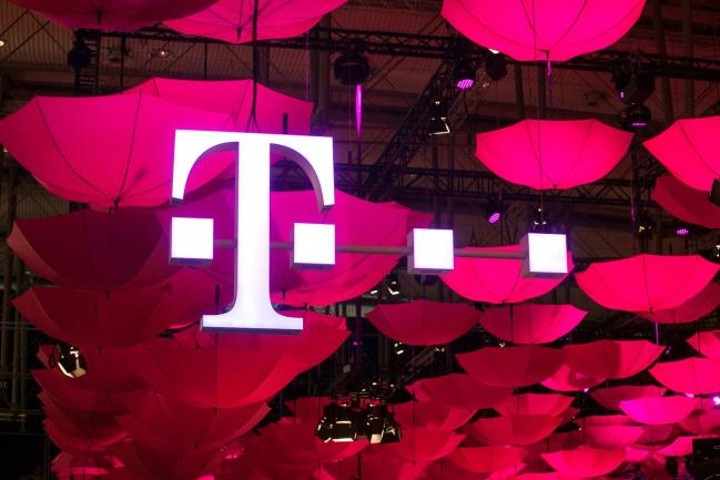© Bloomberg. The T-Mobile logo for Deutsche Telekom AG's T-Systems unit, is seen suspended from the ceiling along with a collection of coloured umbrellas during the CeBit tech show in Hanover, Germany.