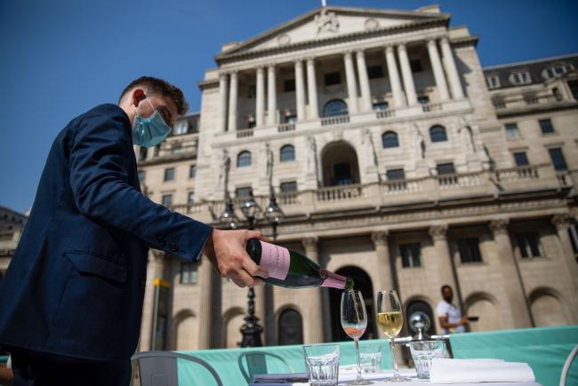 © Bloomberg. A waiter wearing a protective face mask pours champagne at a Fortnum and Mason Plc restaurant outside the Royal Exchange, in view of the Bank of England, in the City of London, U.K., on Tuesday, Sept. 15, 2020. Londoners are steadily increasing their use of public transport after schools reopened, freeing parents to go back to the workplace. Photographer: Simon Dawson/Bloomberg