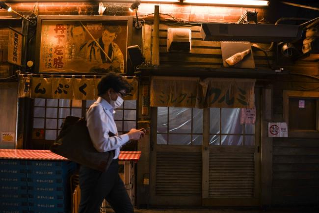 © Bloomberg. A pedestrian wearing a protective mask walks past an izakaya bar in the Shimbashi district of Tokyo, Japan, Friday on May 29, 2020. Small clusters of coronavirus cases have emerged in several locations in Japan, including the capital, in its first week since a state of emergency was lifted nationwide, sparking concern among authorities.