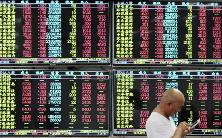 © Reuters. An investor looks at his mobile phone in front of electronic screens showing stock information at a brokerage house in Jiujiang, Jiangxi province, China, August 10, 2015.