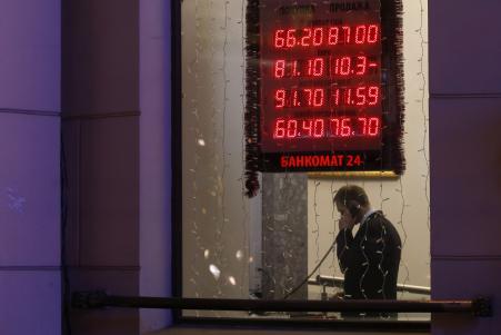 © Reuters. A man talking on a phone is seen in a window of a building with a board showing currency exchange rates on display in the foreground, in Moscow, December 16, 2014.