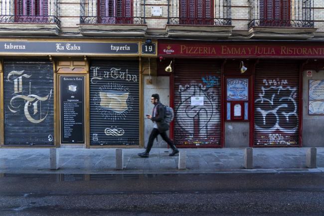 © Bloomberg. A pedestrian walks past a closed tapas bar, left, and restaurant in Madrid, Spain, on Monday, March 16, 2020. The State of emergency declared by the Spanish government to fight the coronavirus outbreak will be extended beyond the 15 days effective from March 14, Transport Minister Jose Luis Abalos said in an interview with state-controlled radio station RNE. Photographer: Angel Navarrete/Bloomberg