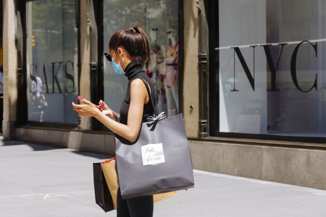 © Bloomberg. A pedestrian wearing a protective mask carries a shopping bag outside the Saks Fifth Avenue store New York, U.S., on Wednesday, June 24, 2020. New York, New Jersey and Connecticut will require visitors from virus hot spots to quarantine for 14 days Photographer: Angus Mordant/Bloomberg