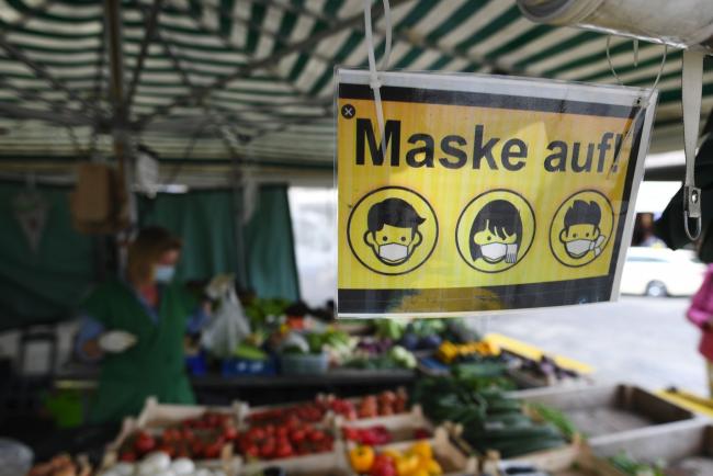 © Bloomberg. A sign tells customer to put a mask on at a fruit and vegetable stall at Viktualienmarkt in Munich, Germany, on Thursday, Sept. 24, 2020. The Bavarian capital city has imposed a five-person limit on gatherings and made mask wearing mandatory in certain public areas in central Munich.