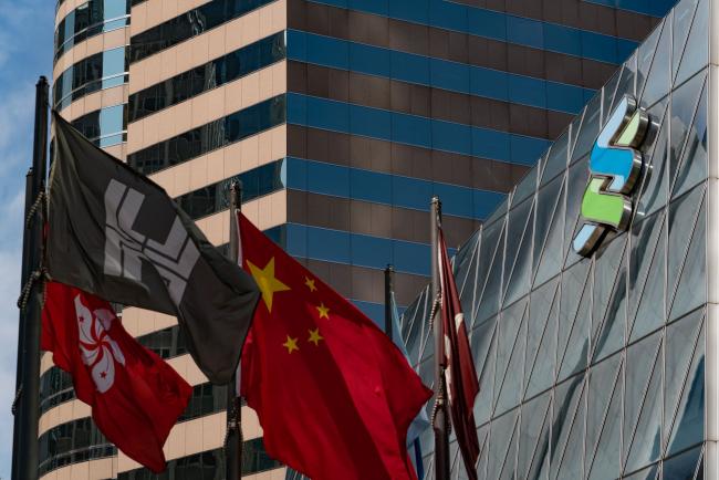 © Bloomberg. The flags of China, center, and the Hong Kong Special Administrative Region, left, flies as the Standard Chartered Plc logo is displayed atop the Standard Chartered Wealth Management Centre in Hong Kong, China, on Saturday, Feb 16, 2019. Standard Chartered is scheduled to release full year earnings results on Feb. 26. Photographer: Anthony Kwan/Bloomberg