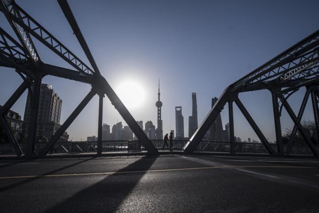 © Bloomberg. Pedestrians walks across a bridge as skyscrapers of the Pudong Lujiazui Financial District stand across the Huangpu River during sunrise in Shanghai, China, on Friday, March 20, 2020. Most of China is now considered low risk and should return to normal work and life, Premier Li Keqiang said at a government meeting on the coronavirus, which is spreading rapidly in Europe, the U.S. and elsewhere. Photographer: Qilai Shen/Bloomberg