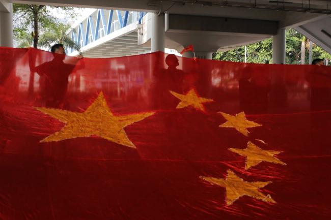 © Bloomberg. Pro-government supporters display a Chinese flag during a flash mob in the Central district of Hong Kong, China, on Tuesday, Oct. 1, 2019. Chinese President Xi Jinping stressed national unity and said relations between Hong Kong and the mainland would improve, as the city braced for a wave of protests to coincide with the 70th anniversary of Communist rule. Photographer: Paul Yeung/Bloomberg
