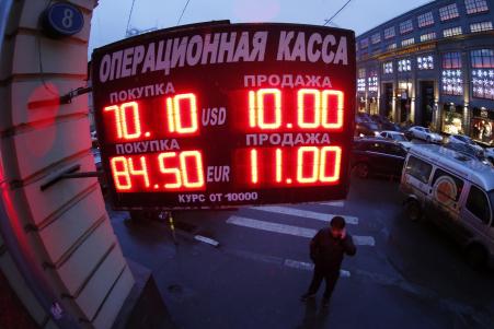 © Reuters. A man stands next to a building under a board showing currency exchange rates in Moscow, December 16, 2014. Russian banks are struggling in the face of a recession.