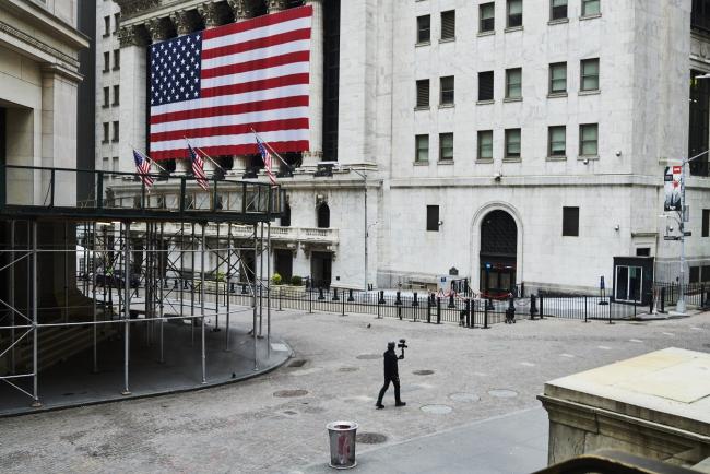 © Bloomberg. A pedestrian films himself while walking past the New York Stock Exchange (NYSE) on a nearly empty Wall Street in the Financial District of New York, U.S., on Monday, March 30, 2020. Roughly 37,500 people have tested positive for the coronavirus in New York City, officials said on Monday, up about 3,700 from a day earlier. Photographer: Gabby Jones/Bloomberg