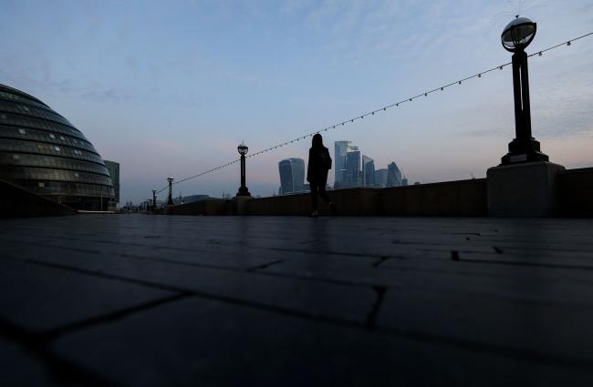 © Bloomberg. A lone pedestrian walks along the Thames Path in view of skyscrapers in the City of London square mile financial district on April 9. Photographer: Simon Dawson/Bloomberg