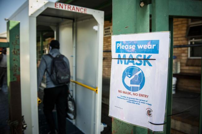 © Bloomberg. A sign advising passengers must wear protective face masks hangs on a beam at the Randburg taxi rank in Johannesburg on May 14. Photographer: Waldo Swiegers/Bloomberg