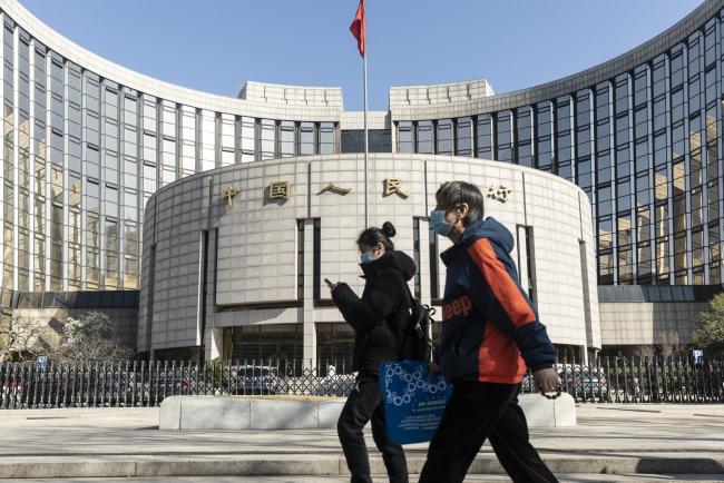 © Bloomberg. Pedestrians wearing protective masks walk past the People's Bank of China (PBOC) building in Beijing, China, on Tuesday, March 17, 2020. China suffered an even deeper slump than analysts feared at the start of the year as the coronavirus shuttered factories, shops and restaurants across the nation, underscoring the fallout now facing the global economy as the virus spreads around the world. Photographer: Qilai Shen/Bloomberg