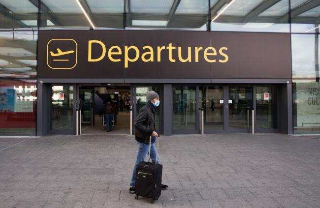 © Bloomberg. A passenger passes the entrance to the departures area at London Gatwick Airport Ltd. in Crawley, U.K., on Saturday, Dec. 19, 2020. The pandemic has put a third of all tourism jobs at risk, and airlines around the world have said they need as much as $200 billion in bailouts. Photographer: Chris Ratcliffe/Bloomberg