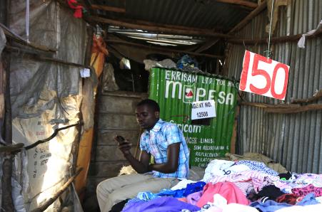 © Reuters/Noor Khamis. Brian Ochieng waits for M-Pesa customers at his second hand clothing shop in Kibera in Kenya's capital Nairobi December 31, 2014. Safaricom, Kenya's biggest telecoms firm, is a model of how technology can be used to financially include millions of people with mobile telephones but without access to traditional infrastructure such as the banks that are available to the wealthy or those living in cities. Safaricom in 2007 pioneered its M-Pesa mobile money transfer technology, now used across Africa, Asia and Europe. It proved that money can be made from people who earn a few dollars a day.