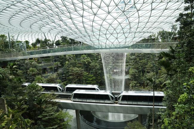 © Bloomberg. Skytrains sit on an elevated platform in front of the Rain Vortex in the Forest Valley garden during a media tour of the Jewel Changi Airport in Singapore, on Thursday, April 11, 2019. The Jewel is a new mega-attraction at Singapore's Changi Airport and will open its doors to the public on April 17. Photographer: Wei Leng Tay/Bloomberg