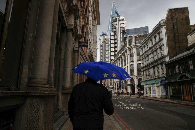 © Bloomberg. A pedestrian holds an umbrella, featuring the design of the European Union (EU) flag, as he shelters from the rain in City of London financial district in London, U.K., on Monday, Aug. 19, 2019. The European Central Bank blasted banks for slow-walking their Brexit preparations, telling them to move additional staff and resources to the European Union in case Britain leaves without a deal on Oct. 31.