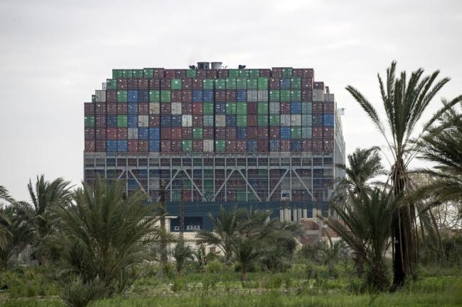 © Bloomberg. SUEZ, EGYPT - MARCH 28: The container ship, the Ever Given, is seen from a village near the Suez Canal on March 28, 2021 in Suez, Egypt. Work continues to free the Ever Given, a huge container ship stuck sideways in Egypt's Suez Canal. The ship ran aground in the canal on March 23, after being caught in 40-knot winds. Dredgers have been working on the port side of the ship in an attempt to remove sand and mud and dislodge the vessel. The Suez Canal is one of the worlds busiest shipping lanes and the blockage has created a backlog of vessels at either end, raising concerns over the impact the accident will have on global shipping and supply chains. (Photo by Mahmoud Khaled/Getty Images)