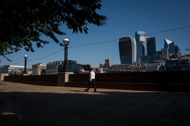 © Bloomberg. A pedestrian walks in view of skyscrapers, including 20 Fenchurch Street, also known as The Walkie Talkie, 22 Bishopgate, The Leadenhall Building, also known as The Cheesegrater, The Scalpel, and 30 St. Mary's Axe, also known as the Gherkin, in London, U.K., on Friday, July 31, 2020. London's best offices are forecast to plunge in value by as much as 15% this year as the coronavirus hits rents and investors' appetite for real estate.